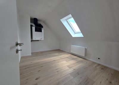 Pièce sous combles du projet Maison Braine-l'Alleud, nouvelle construction avec fenêtre de toit Velux, parquet clair et unité de ventilation.